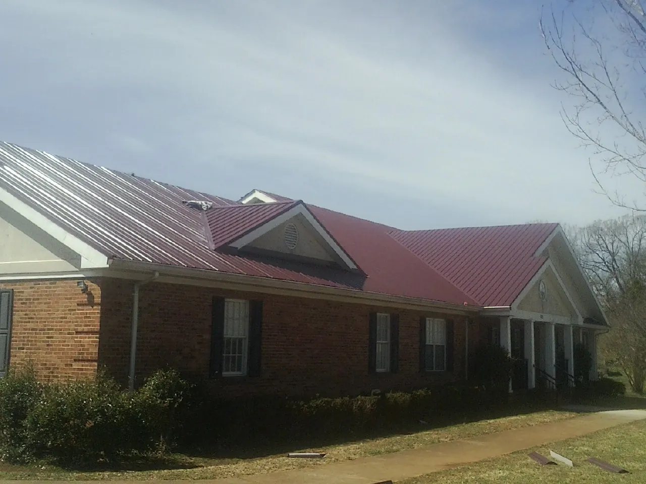 Red metal roof with gabled entries on a long brick building, from a Hail Damage Roof Repair job in Mount Hood Parkdale