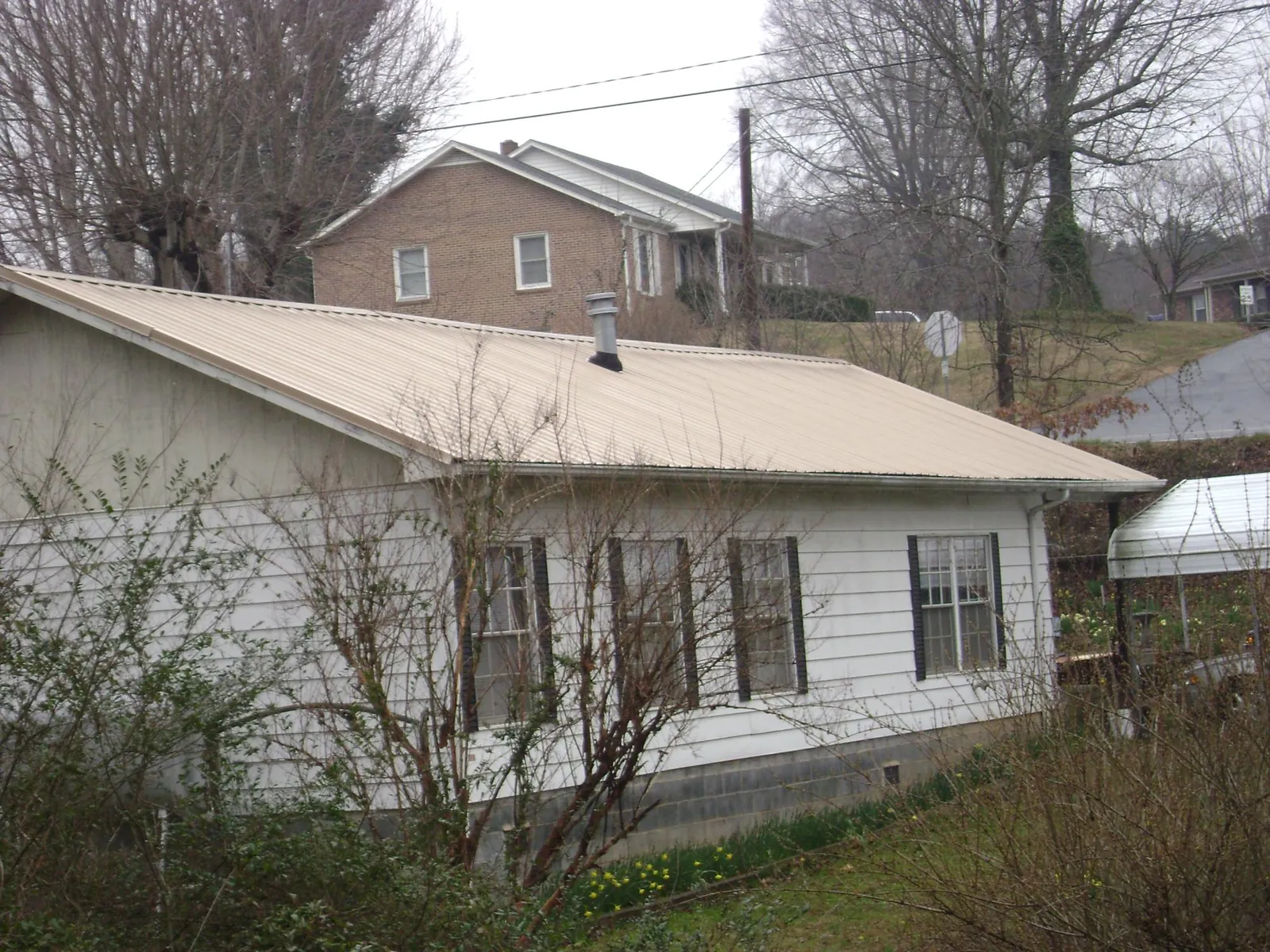 Tan metal roof on a white sided house set into a hillside — Commercial Roofing by Roofing Brothers in Mount Hood Parkdale